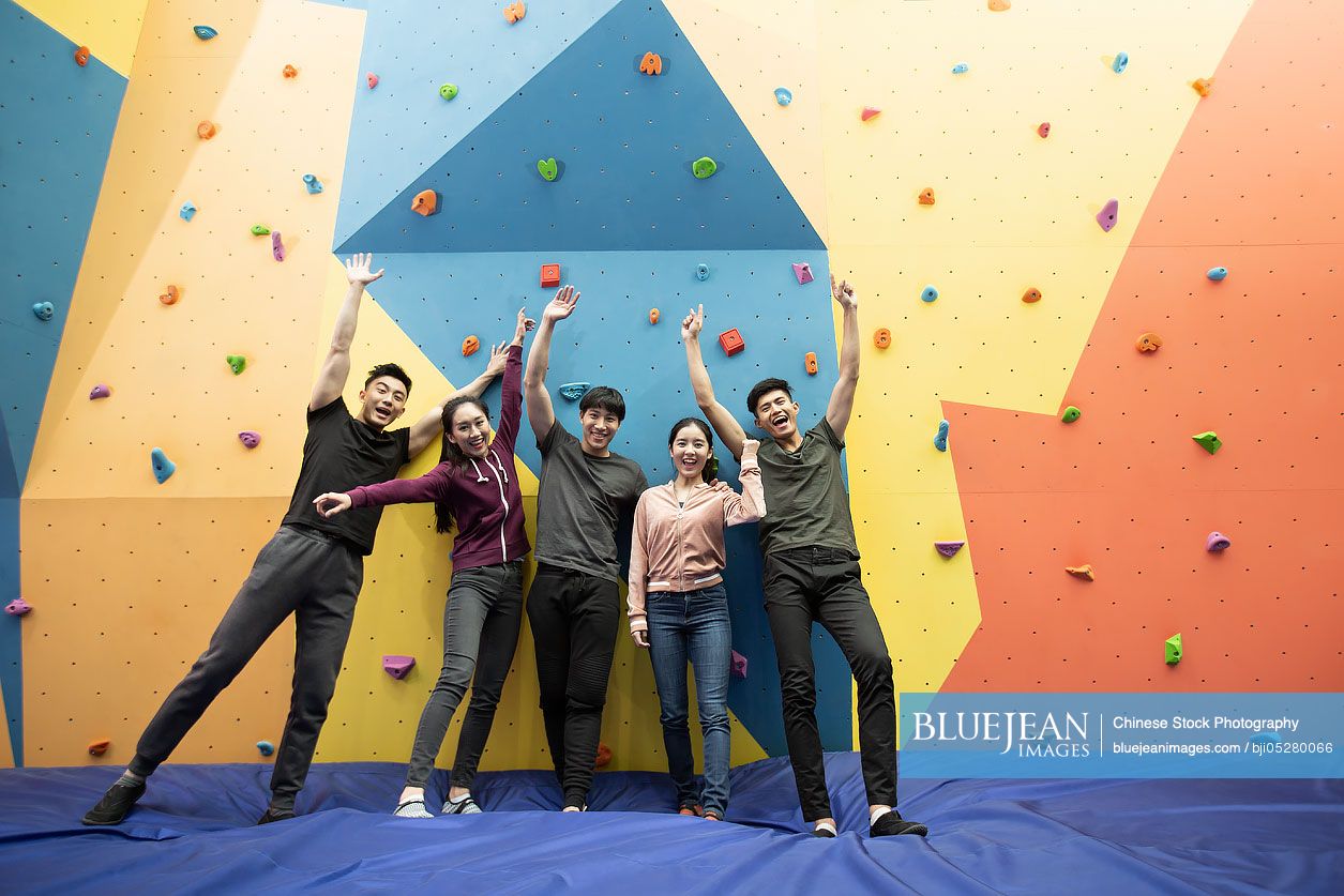 Happy young Chinese friends standing against climbing wall at gym