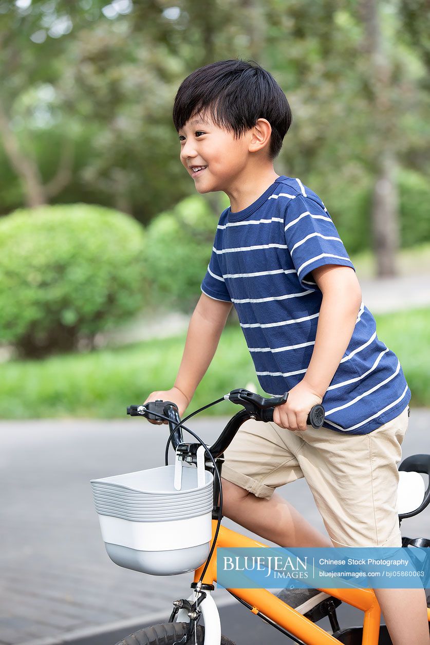 Happy little Chinese boy riding bike in park