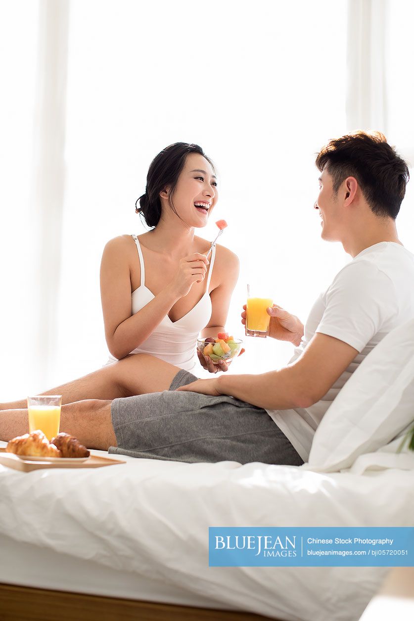 Happy young Chinese couple having breakfast on bed