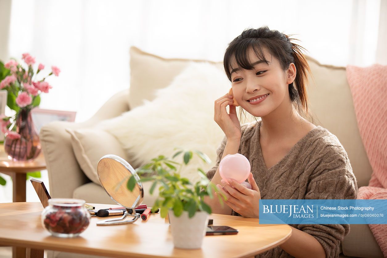 Young Chinese woman applying makeup at home