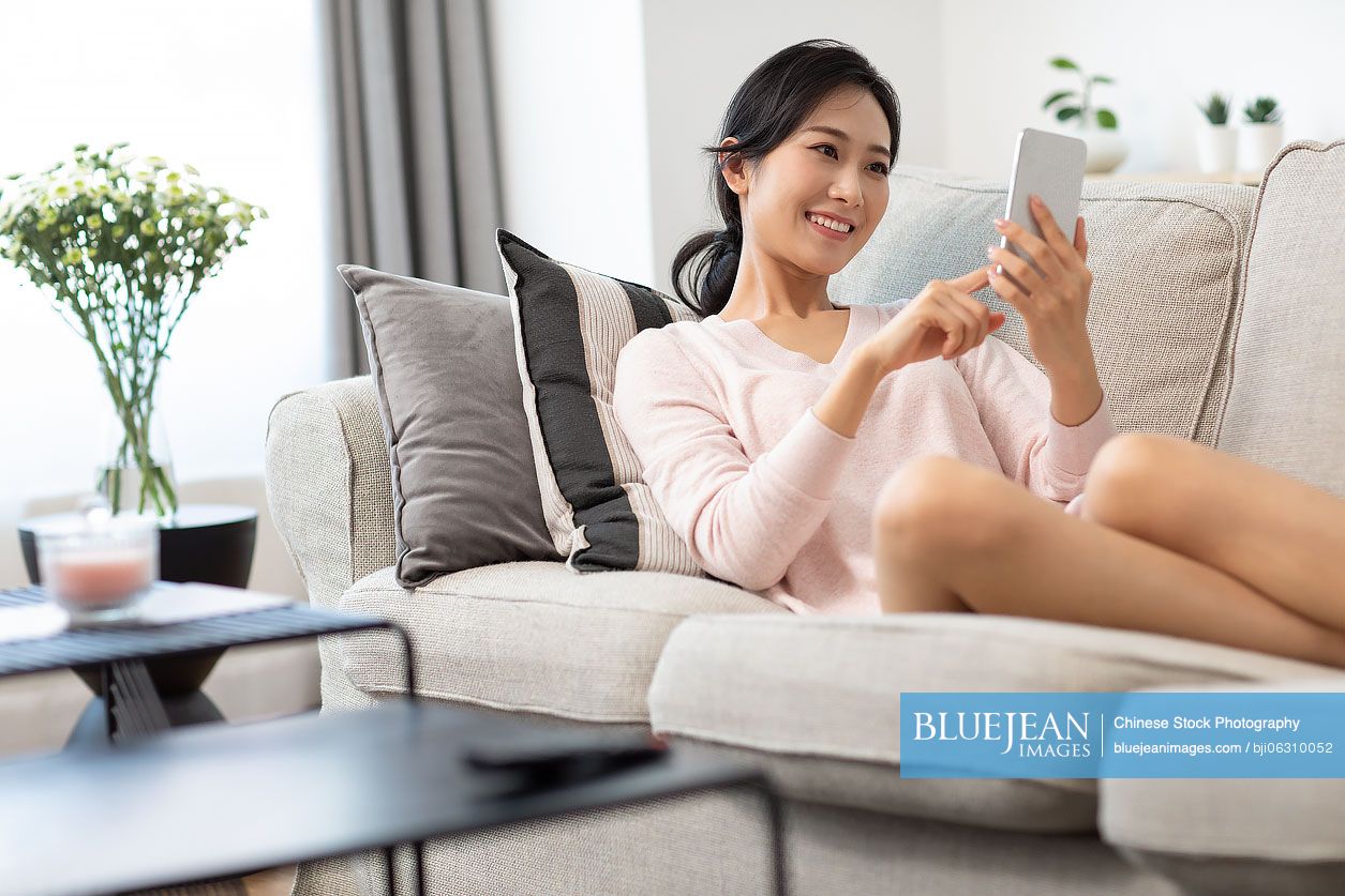 Happy young Chinese woman using smartphone in living room