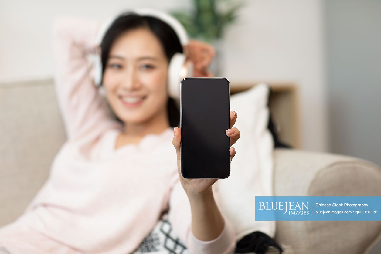 Happy young Chinese woman wearing headphones on sofa