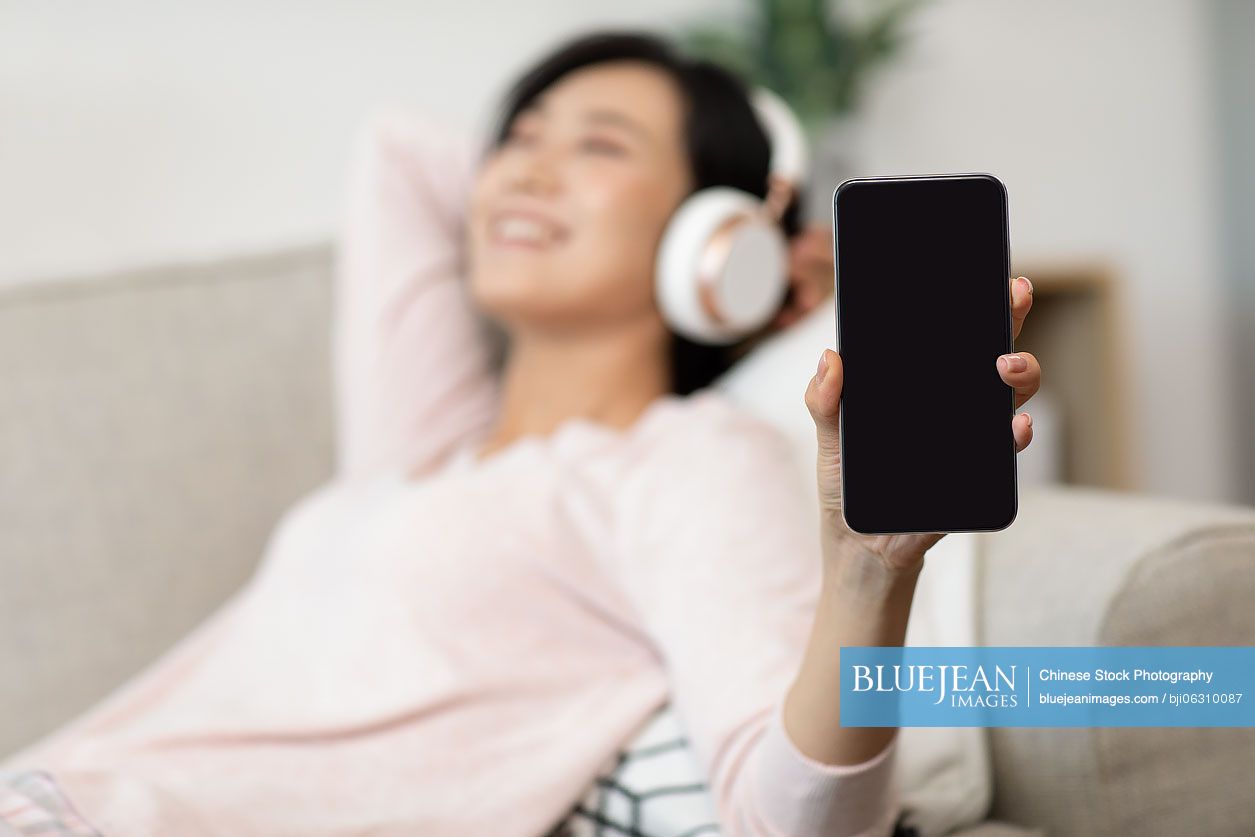 Happy young Chinese woman wearing headphones on sofa