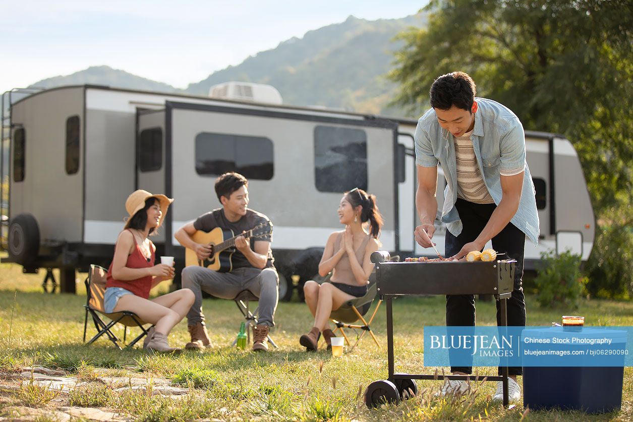 Happy young Chinese friends barbecuing outdoors