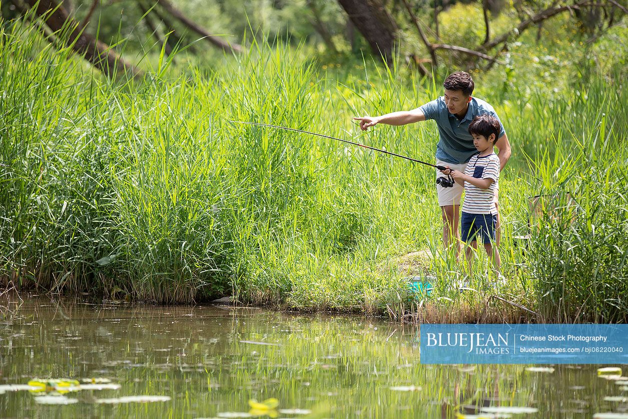 Happy Chinese father and son fishing by the river