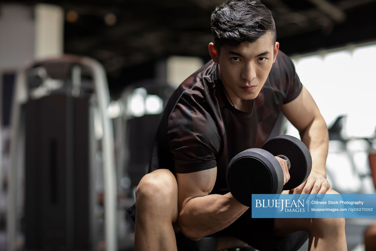 Young Chinese man working out with dumbbell at gym