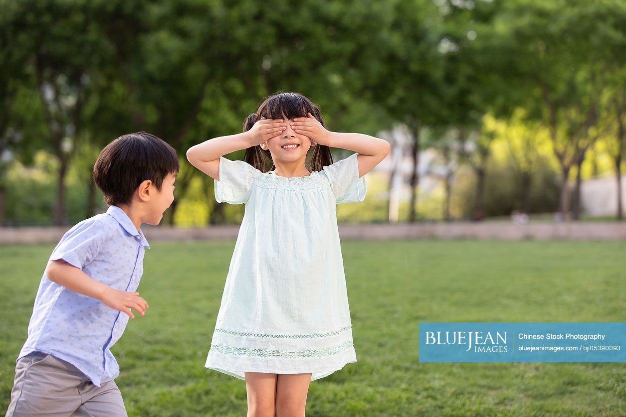 Two Chinese children playing hide and seek in park