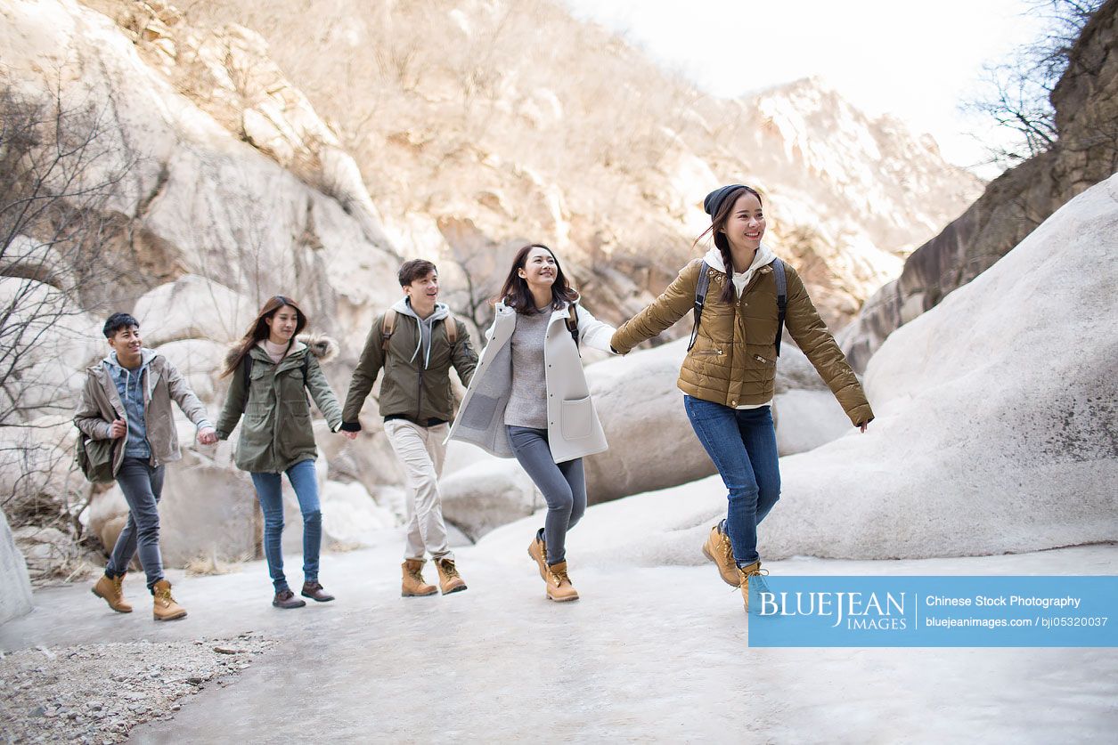 Happy young Chinese friends holding hands running outdoors in winter