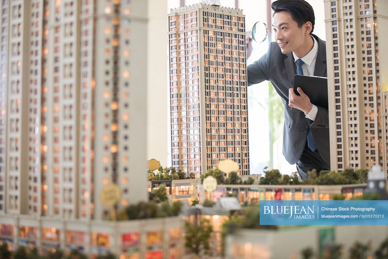 Chinese realtor checking architectural model through magnifying glass