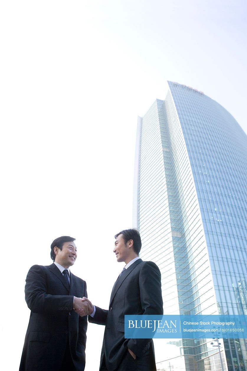 Chinese businessmen shaking hands in front of tall building