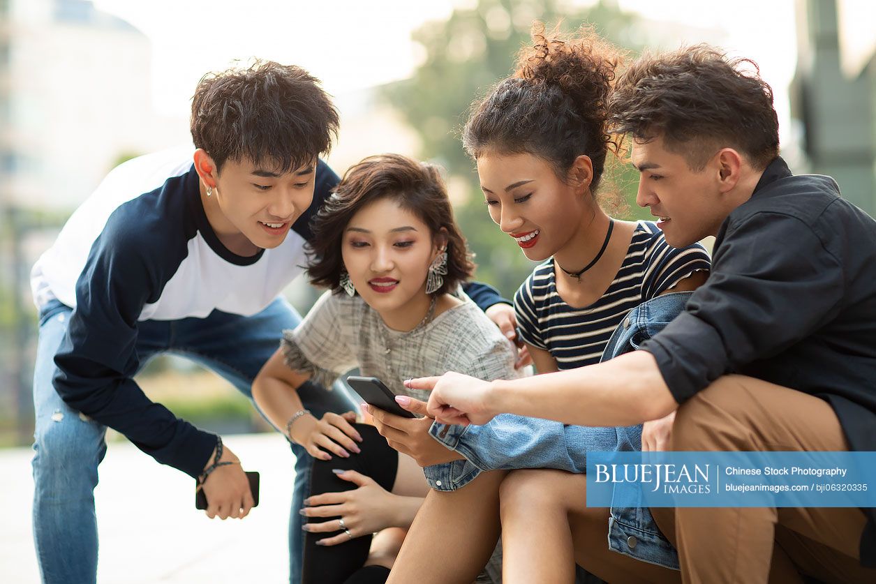 Happy young Chinese friends using smartphone outdoors