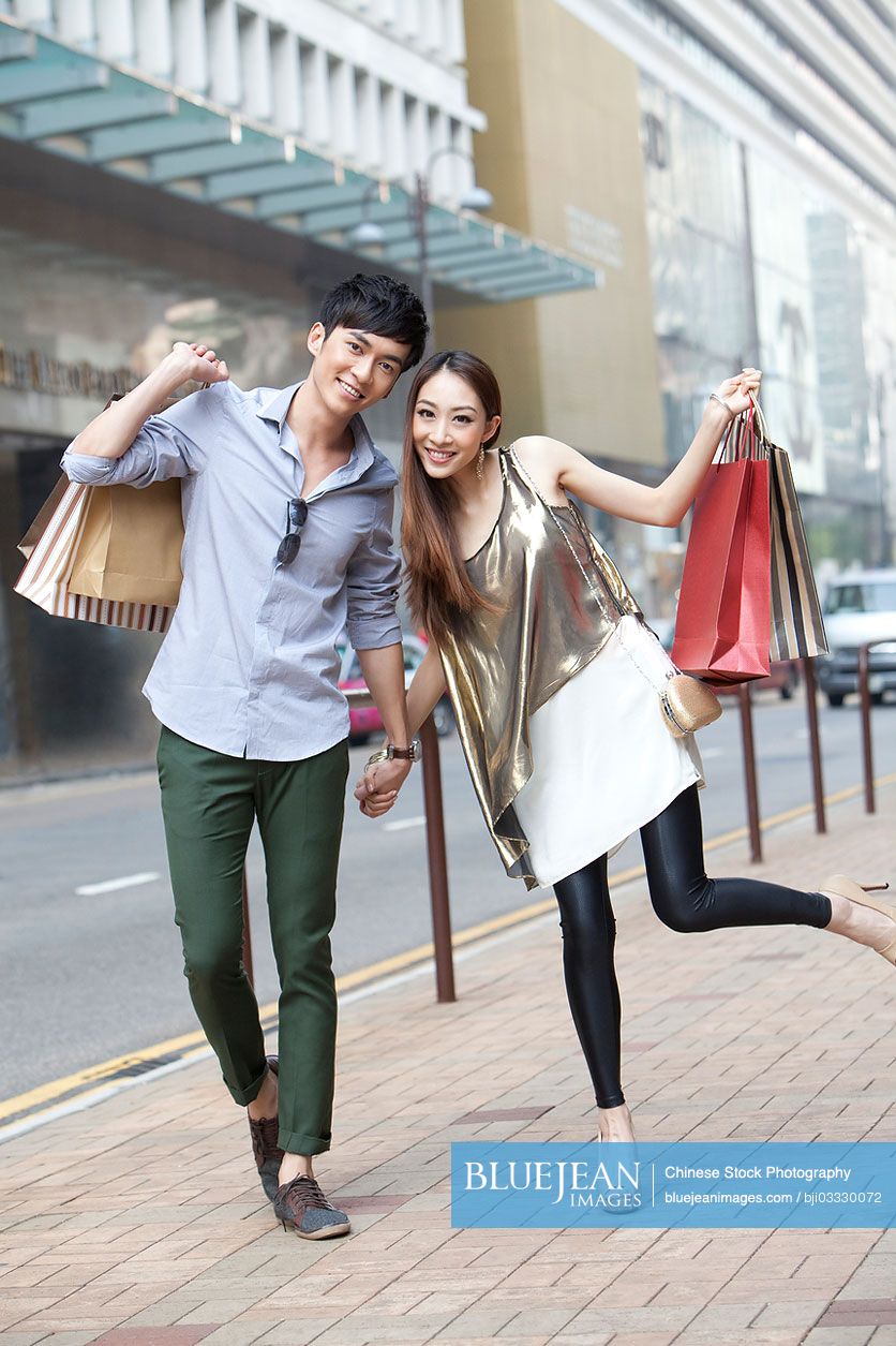 Cheerful young Chinese couple with shopping bags in hand on the street of Hong Kong