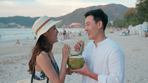 快乐的年轻情侣在沙滩喝椰汁