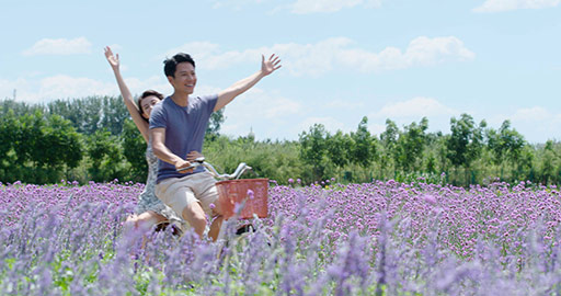 Happy young Chinese couple riding bike by flower field,4K