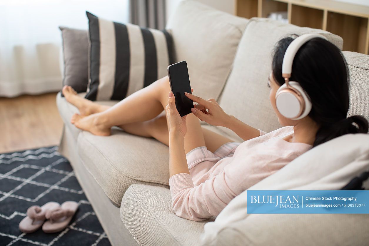 Young Chinese woman using smartphone on sofa