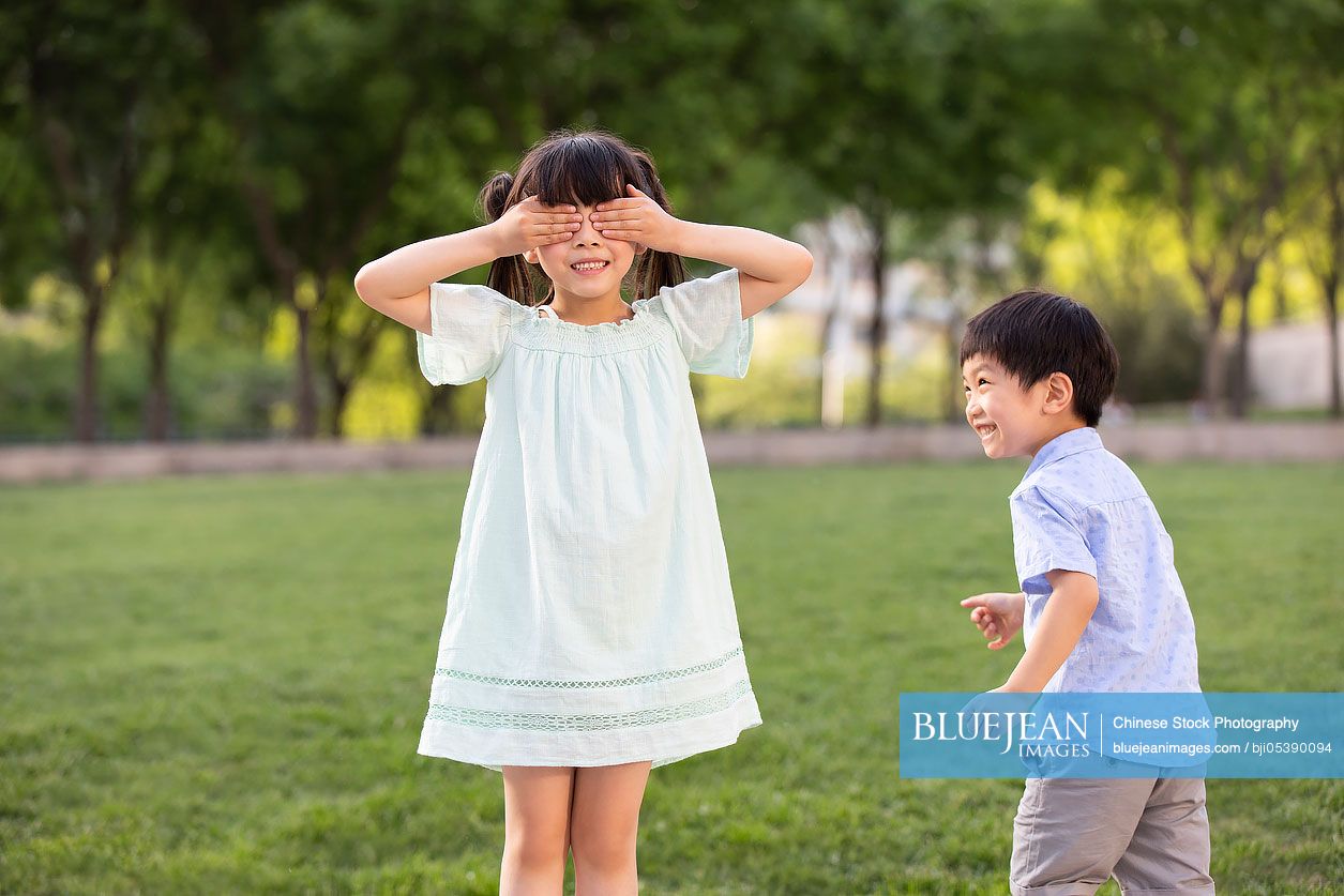 Two Chinese children playing hide and seek in park