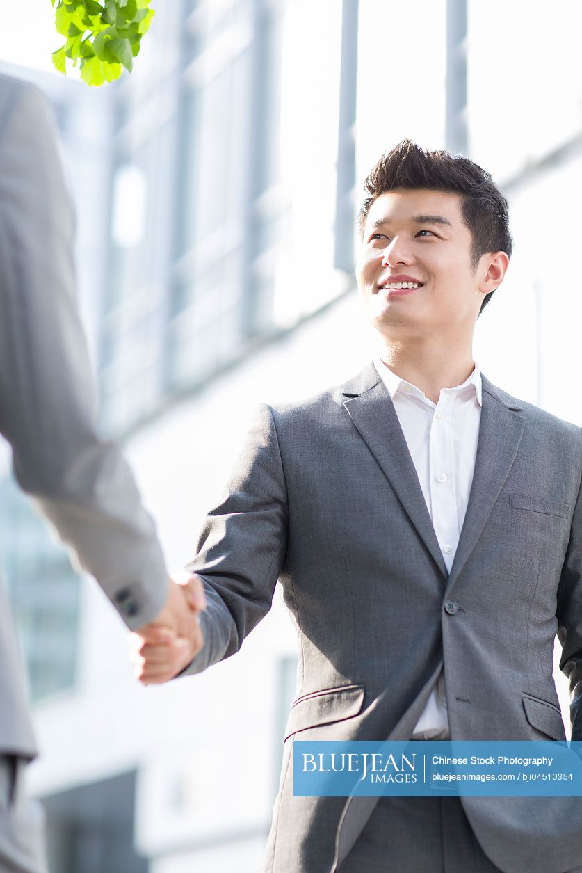 Young Chinese business person shaking hands outdoors