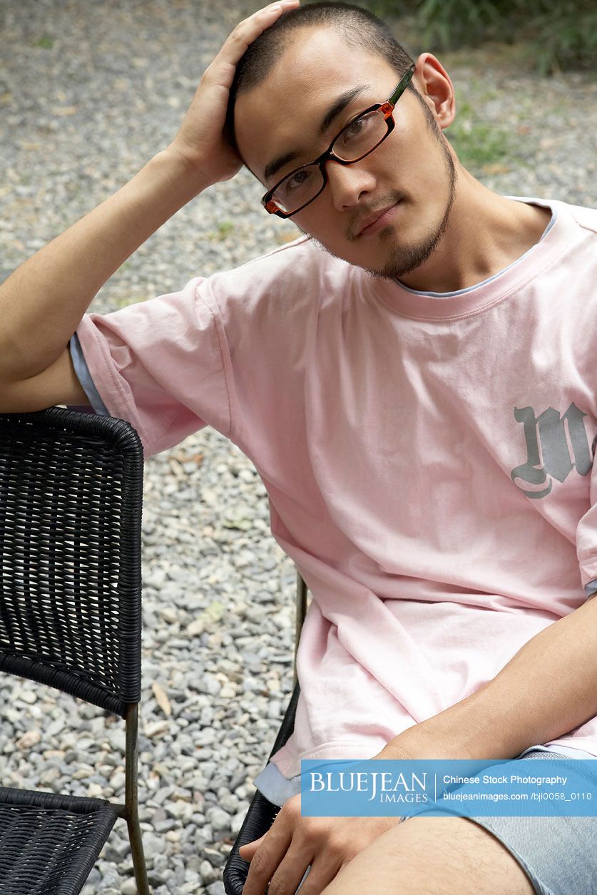 Young Chinese man sitting down leaning on chair looking at camera