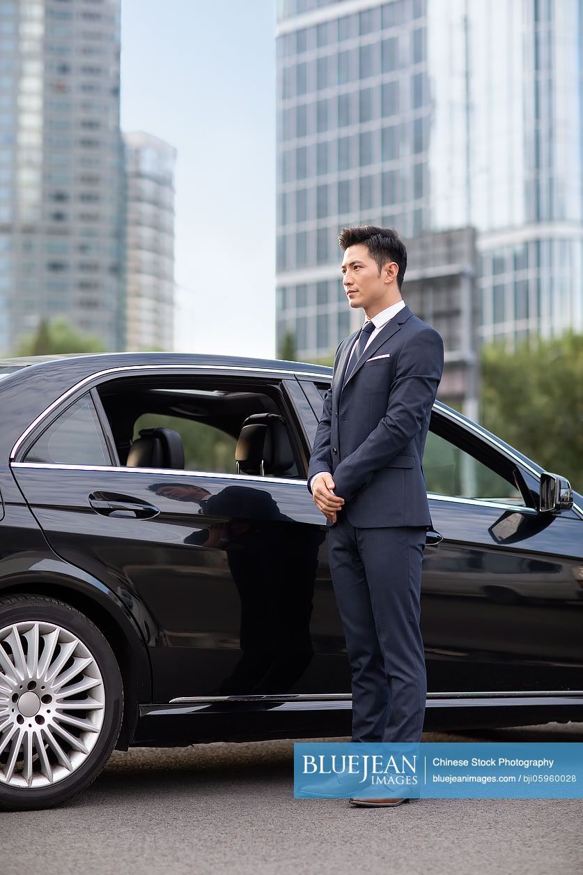 Young Chinese chauffeur standing next to a car