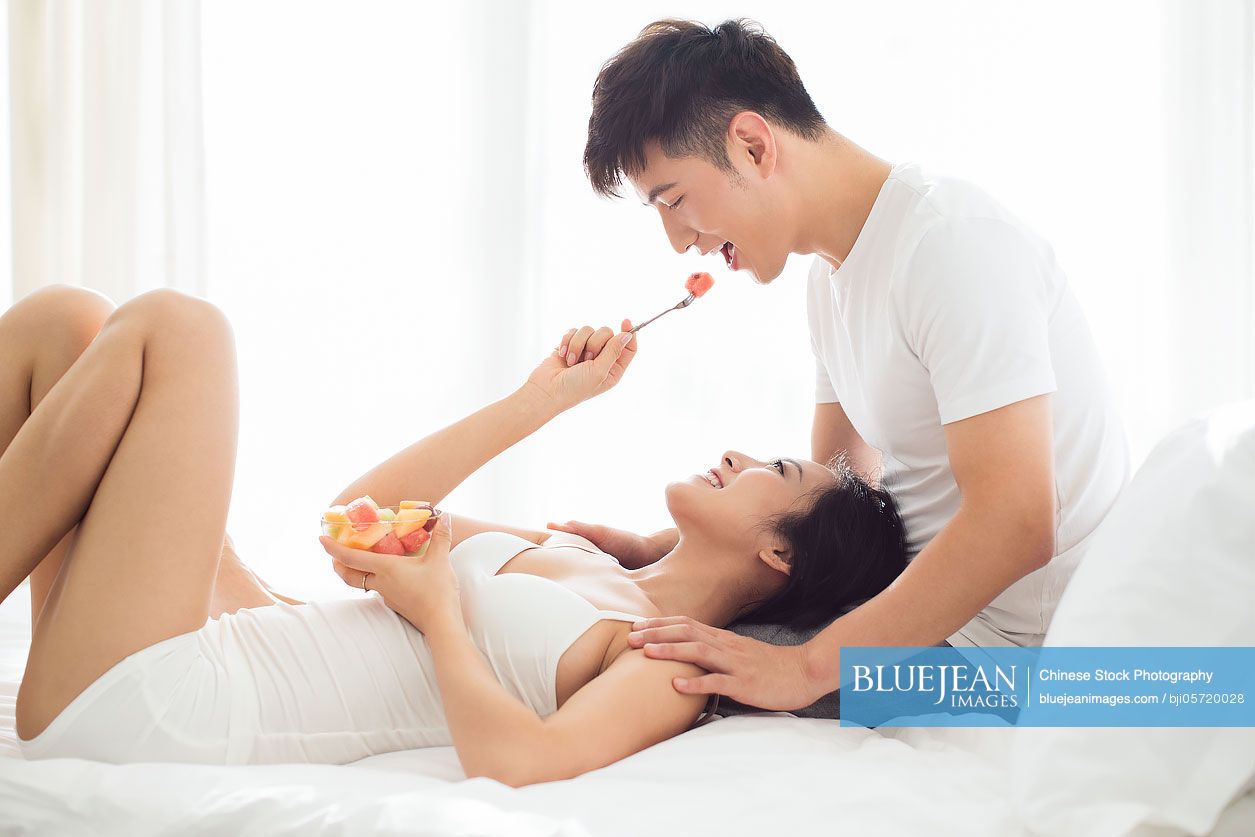 Happy young couple eating fruit salad on bed