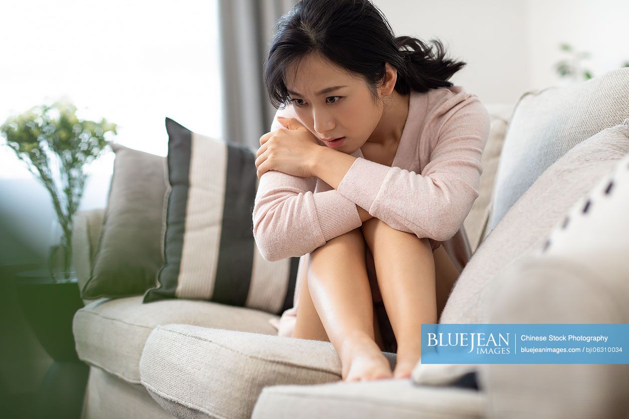 Unhappy young Chinese woman on sofa
