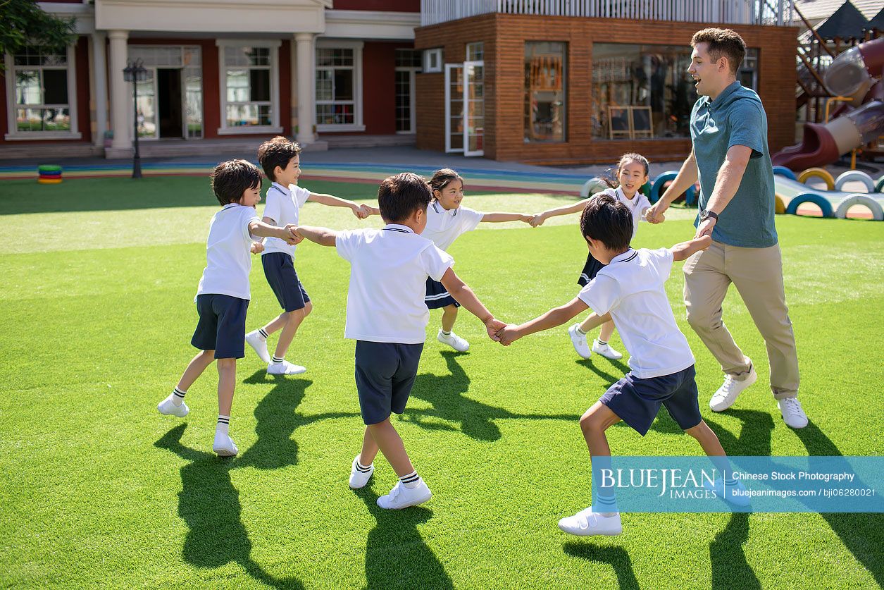 Foreign teacher and children playing in kindergarten playground