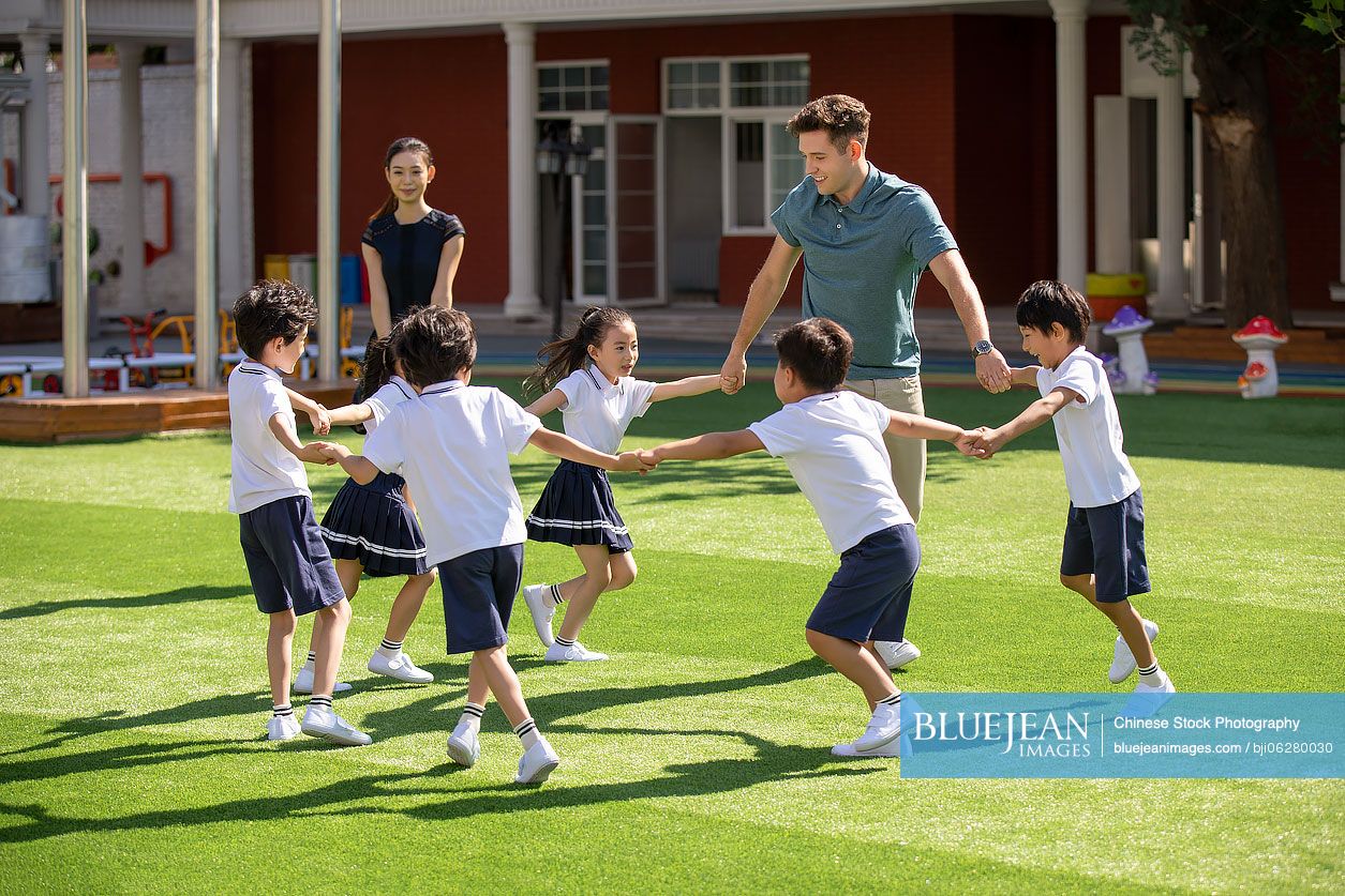 Teachers and children playing in kindergarten playground