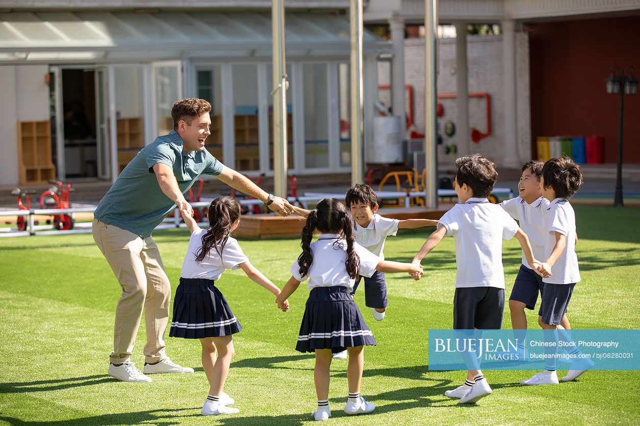 Foreign teacher and children playing in kindergarten playground