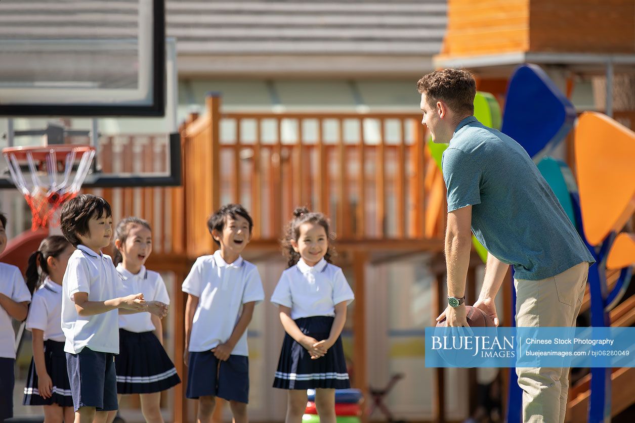 Foreign teacher teaching children basketball in playground