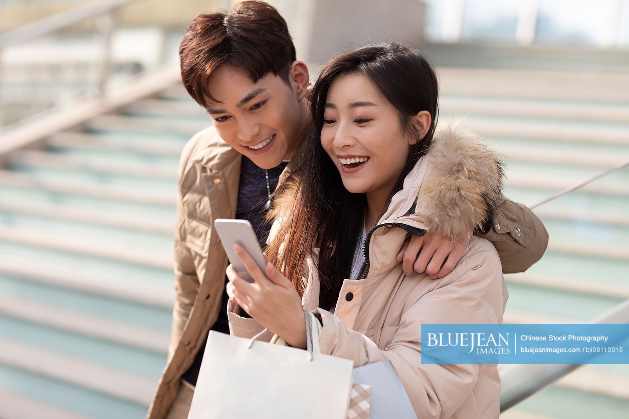 Happy young Chinese couple using smartphone outdoors