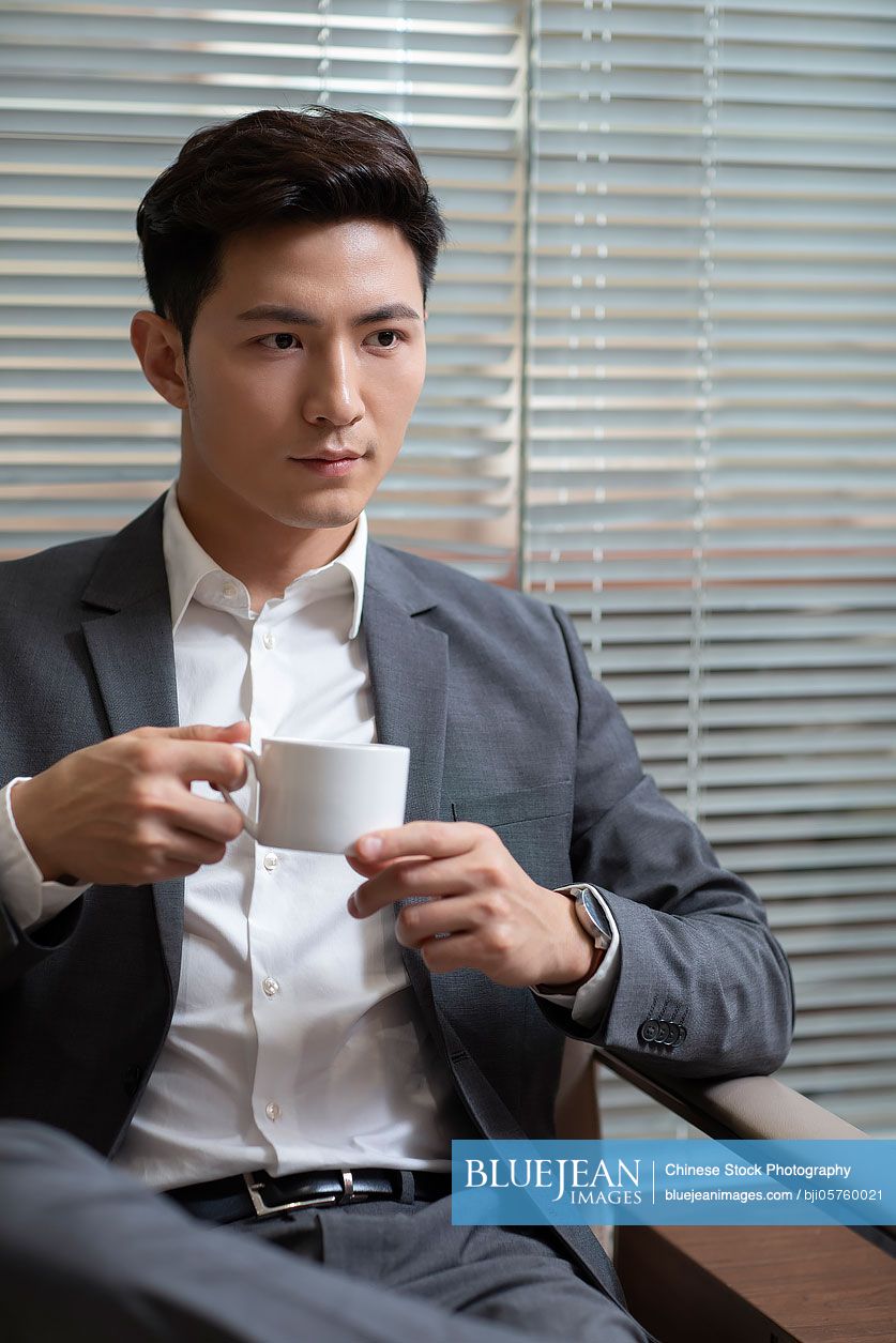 Confident Chinese businessman drinking coffee in office