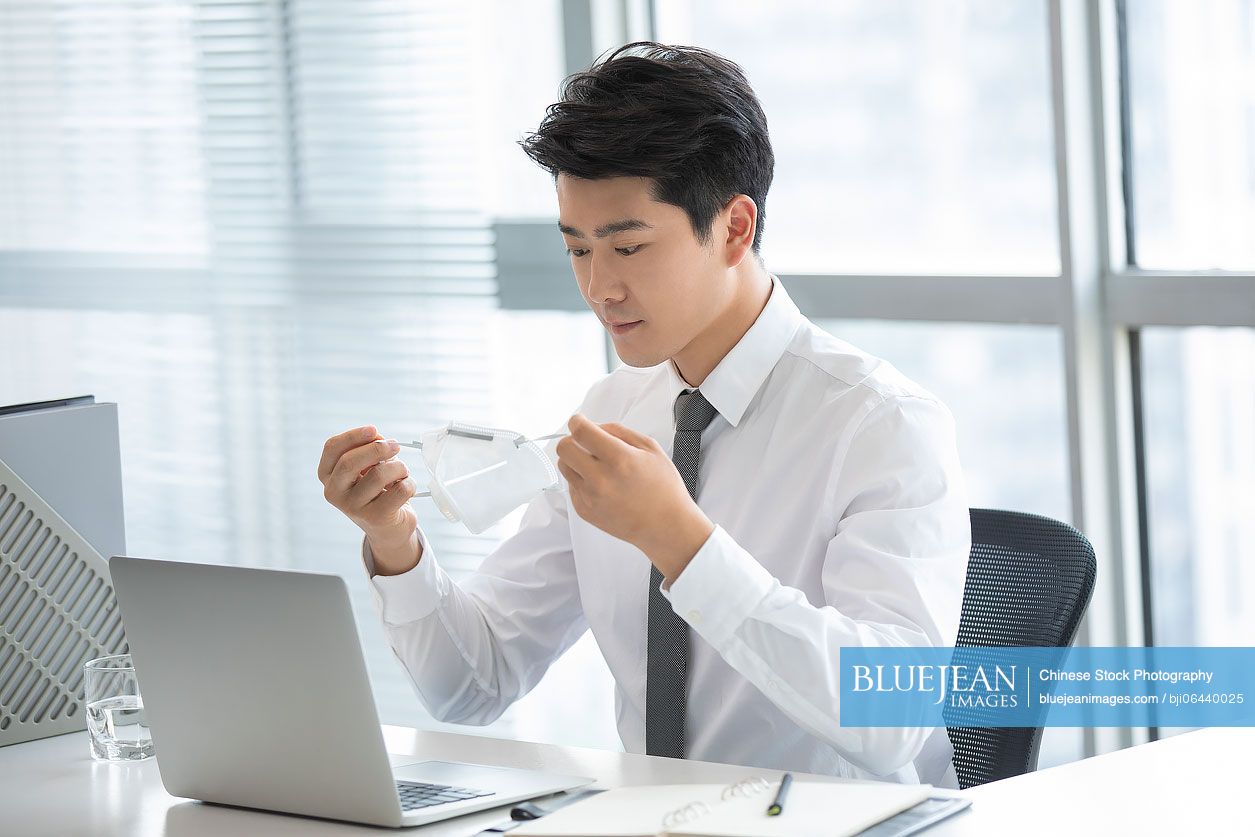 Young Chinese businessman wearing N95 mask in office