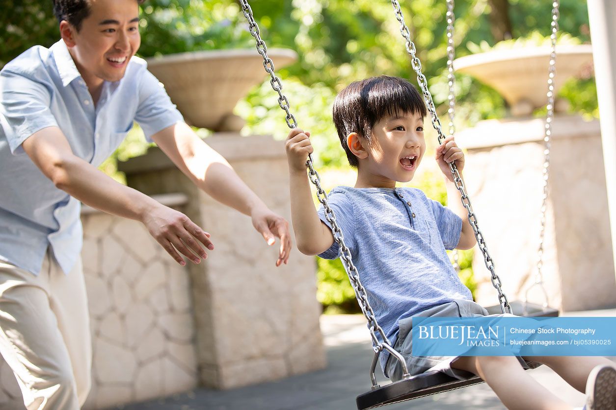 Happy young Chinese father pushing son on swing