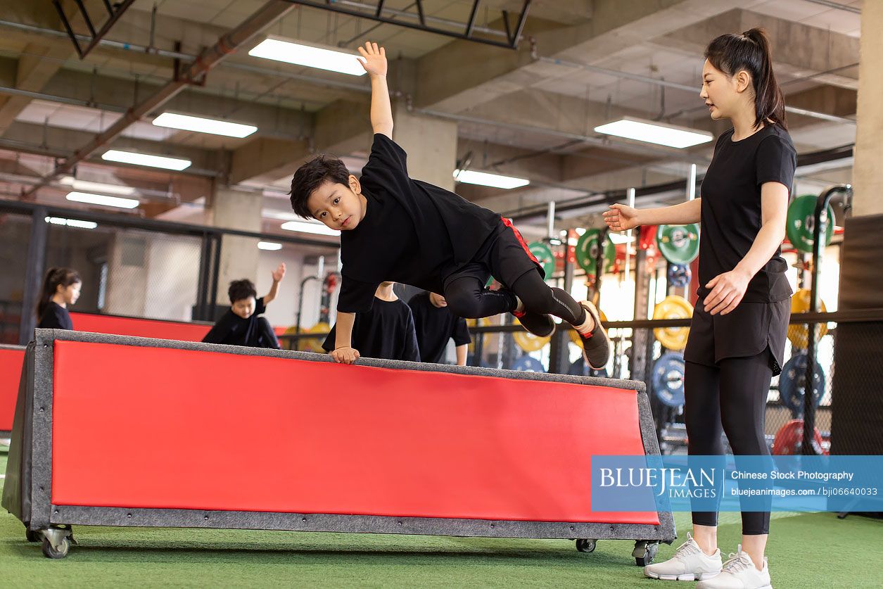 Active Chinese children having exercise class with their coach in gym