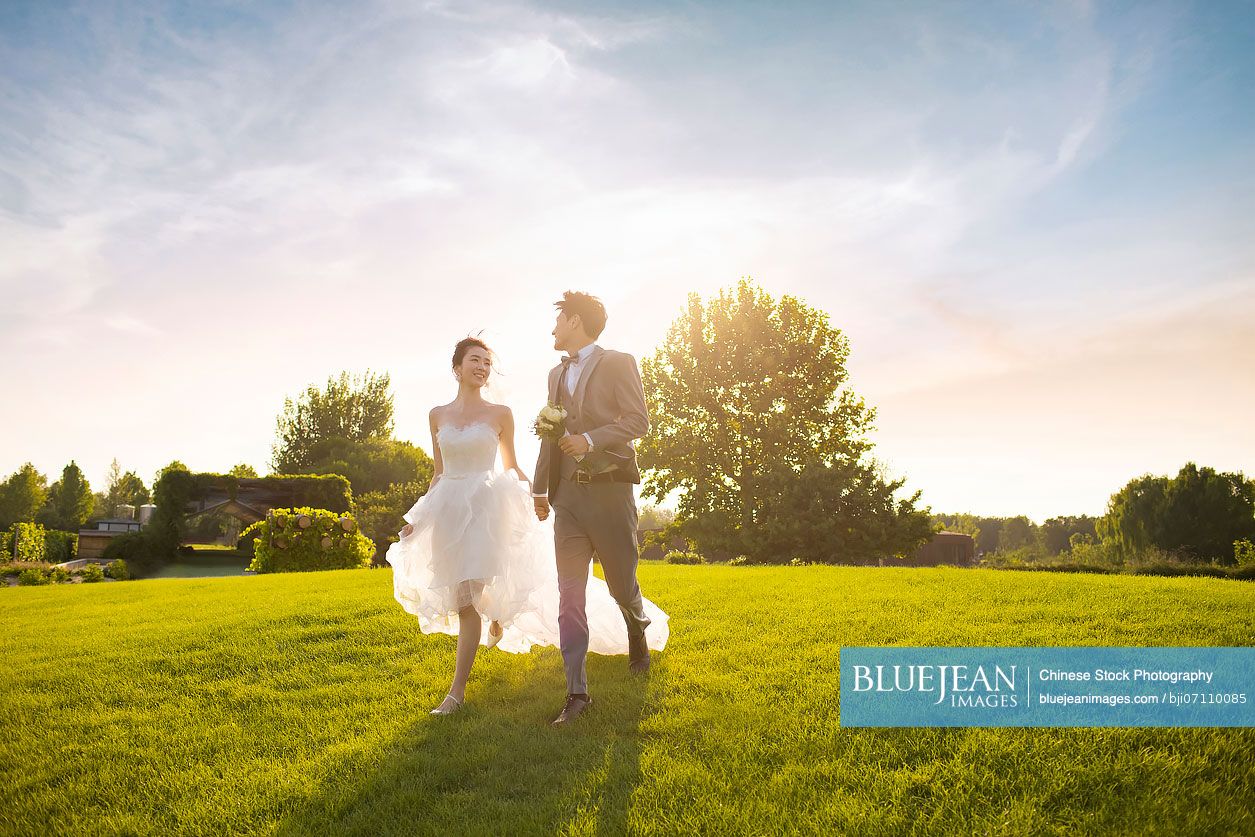 Happy Chinese bride and groom running on the grass