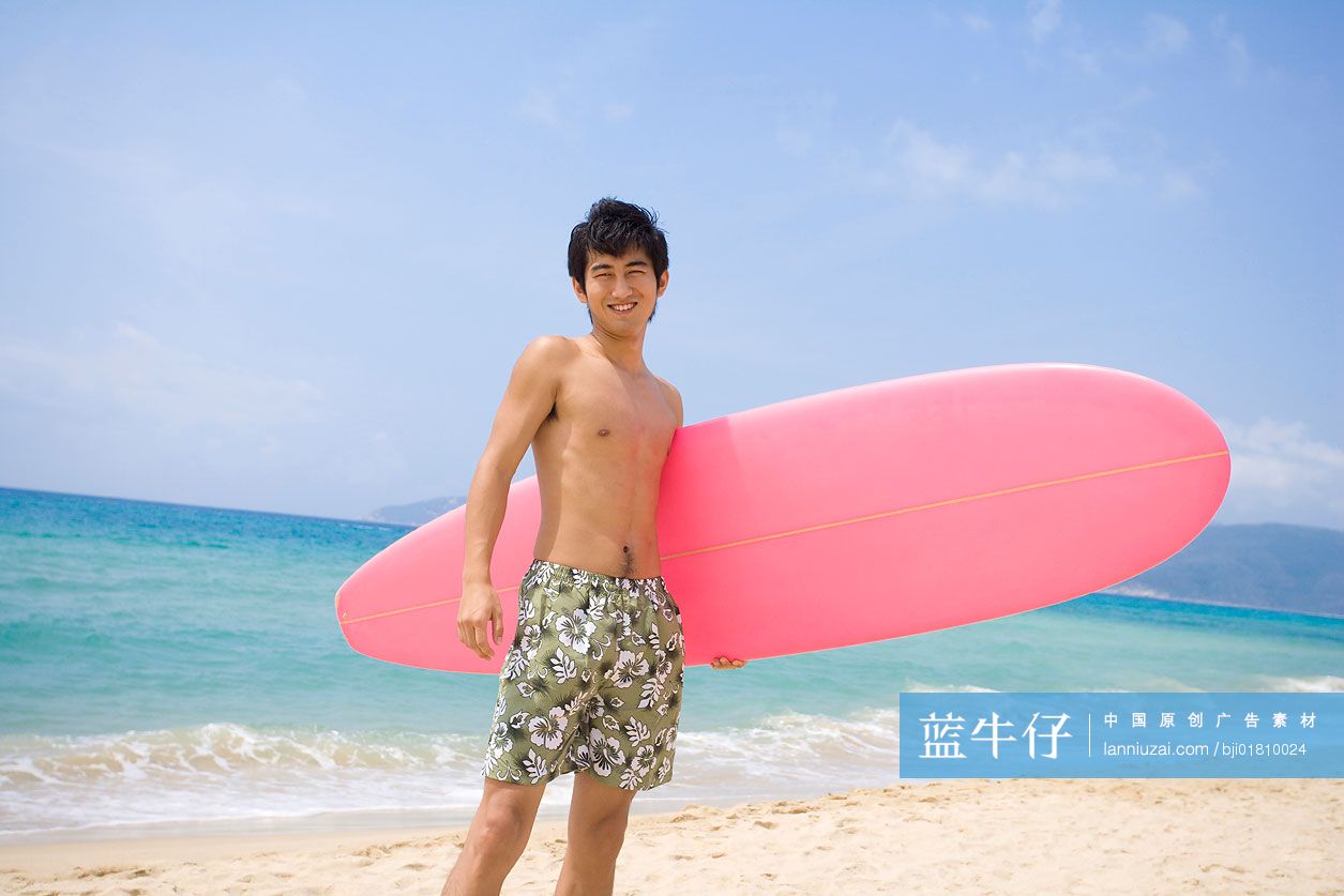 拿着冲浪板的男孩站在沙滩上