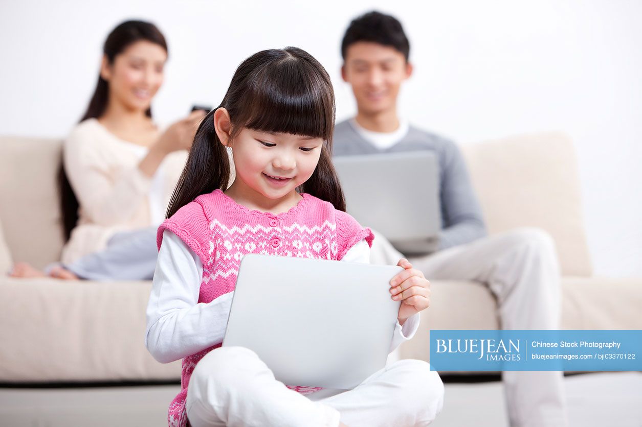 Young Chinese family using electronic gadgets in living room