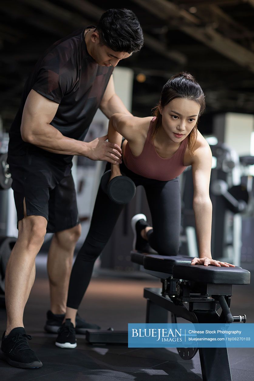 Young Chinese woman working out with personal trainer at gym
