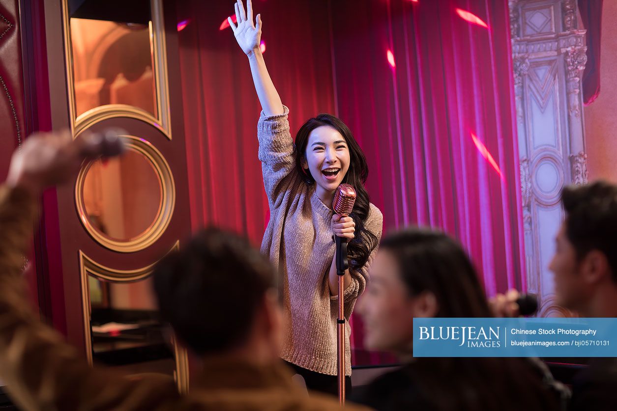 Happy young Chinese woman singing karaoke in nightclub