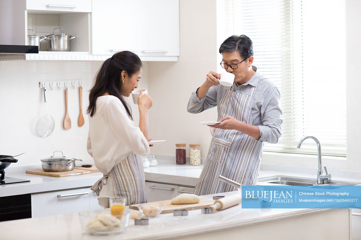 Happy mature Chinese couple drinking coffee in kitchen