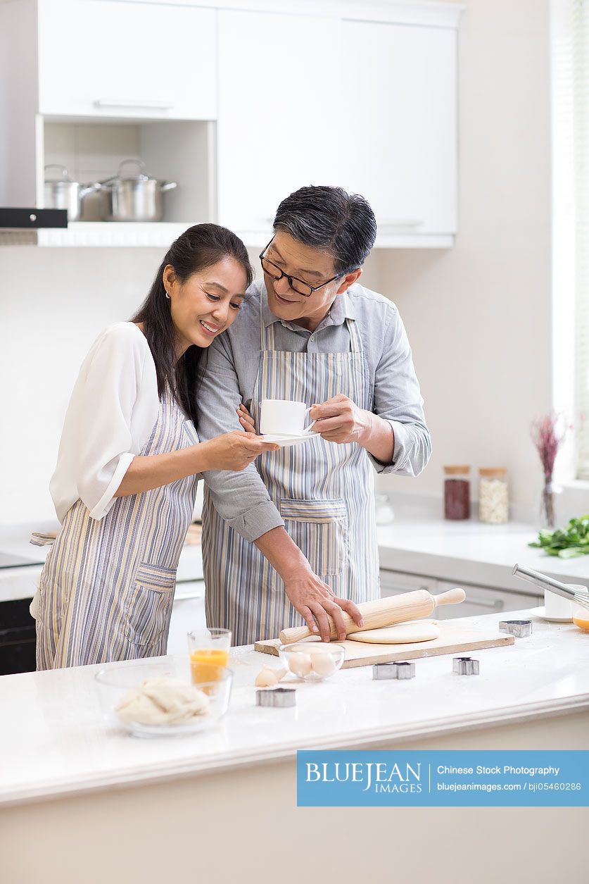 Happy mature Chinese couple baking cookies in kitchen