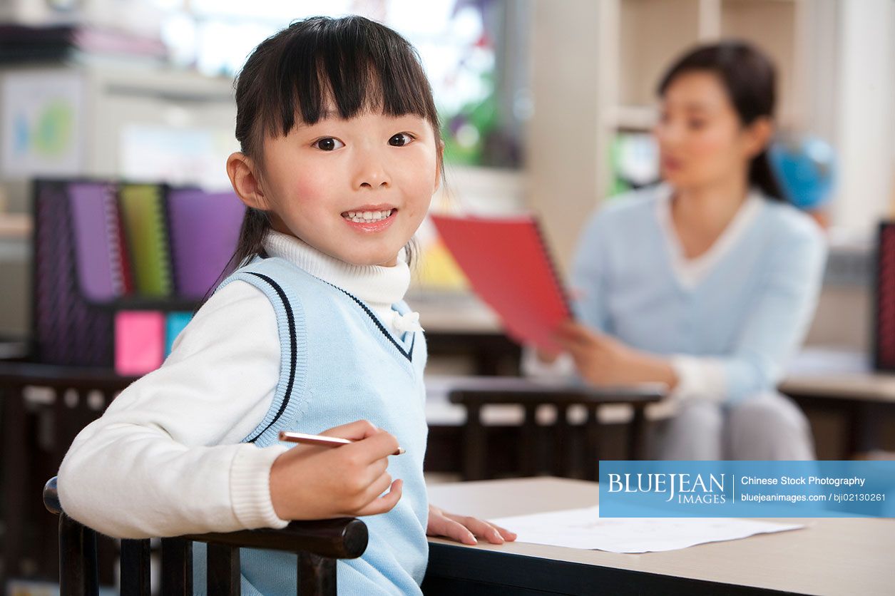 Young Chinese student looking over shoulder and smiling in class