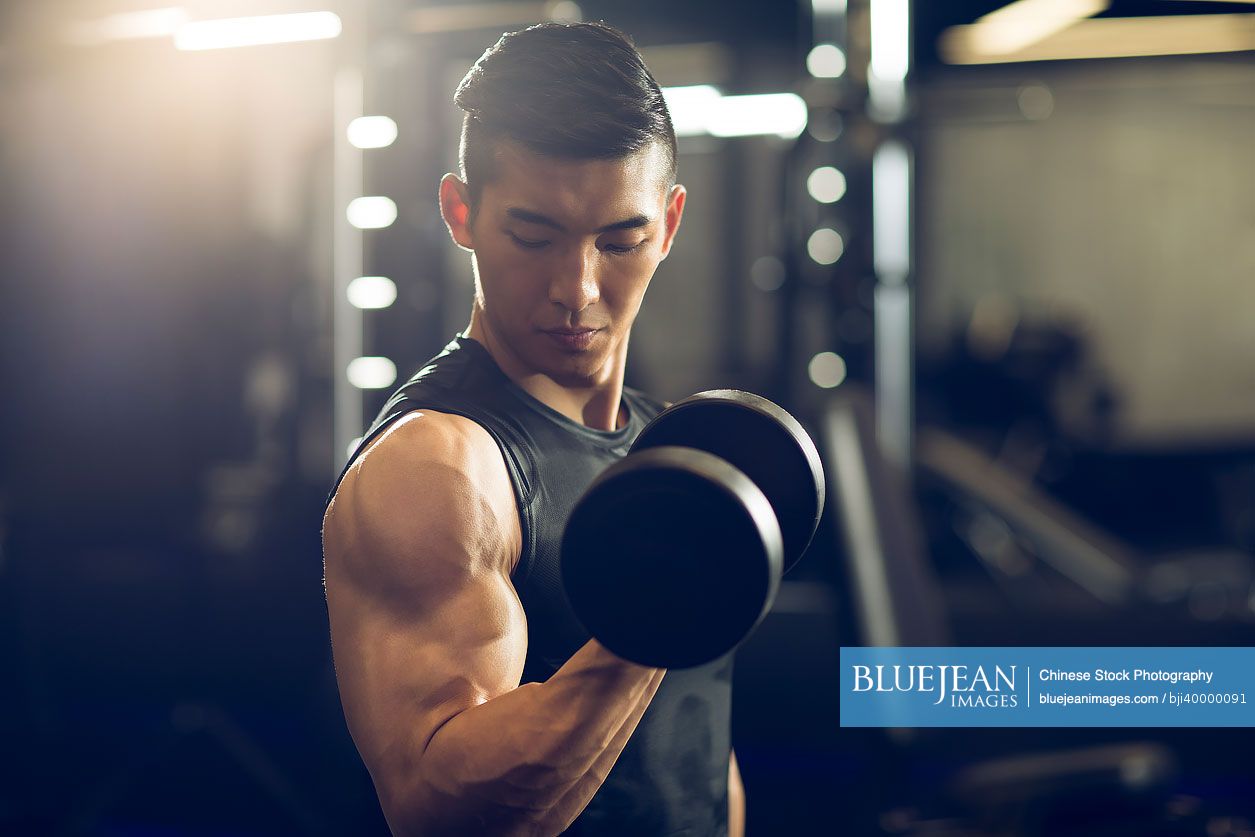 Young Chinese man working out with dumbbell at gym