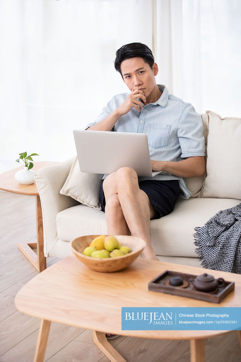 Happy young Chinese man using laptop in living room