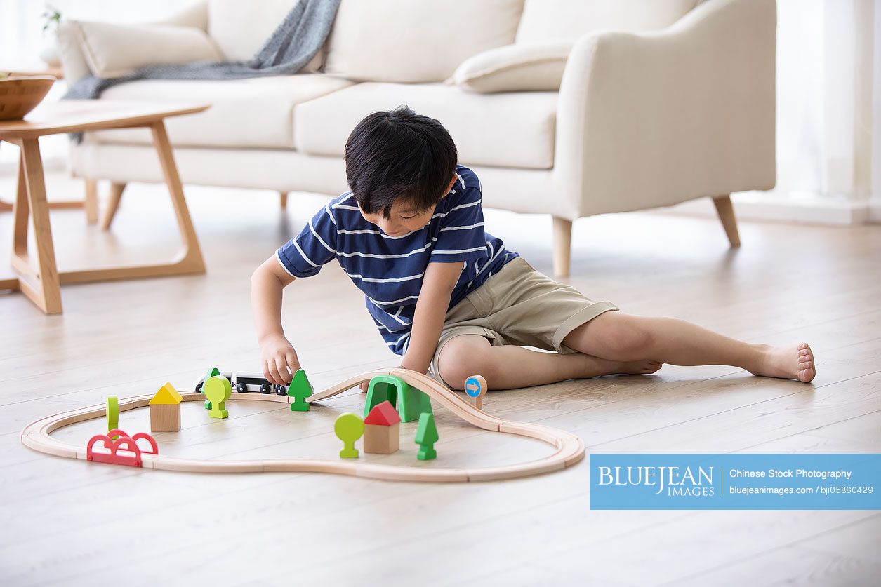 Little Chinese boy playing with toy train on floor