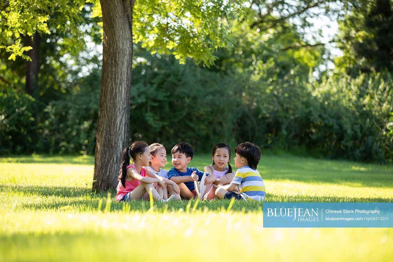 Happy Chinese children reading book on meadow