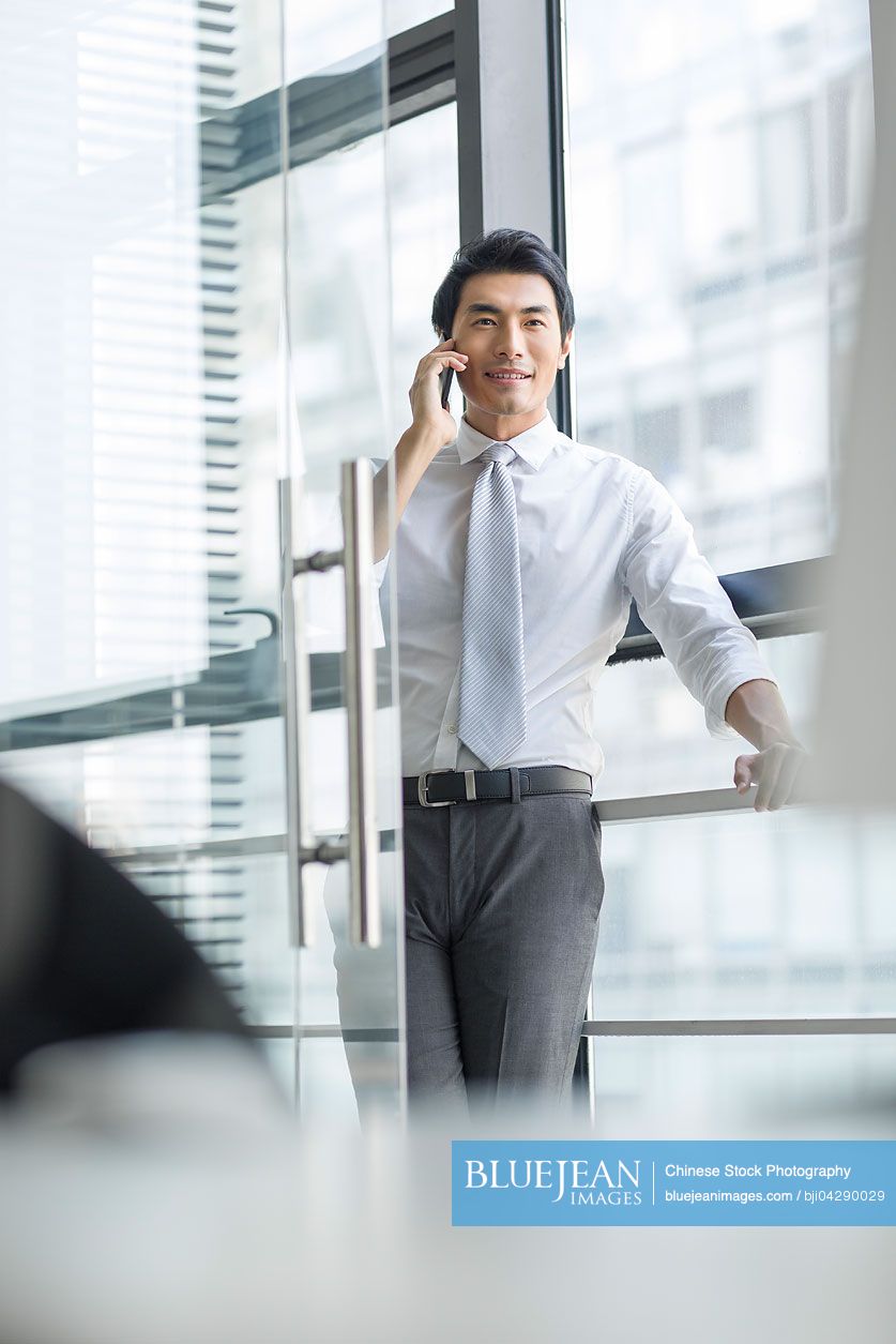 Young Chinese businessman talking on cell phone in office