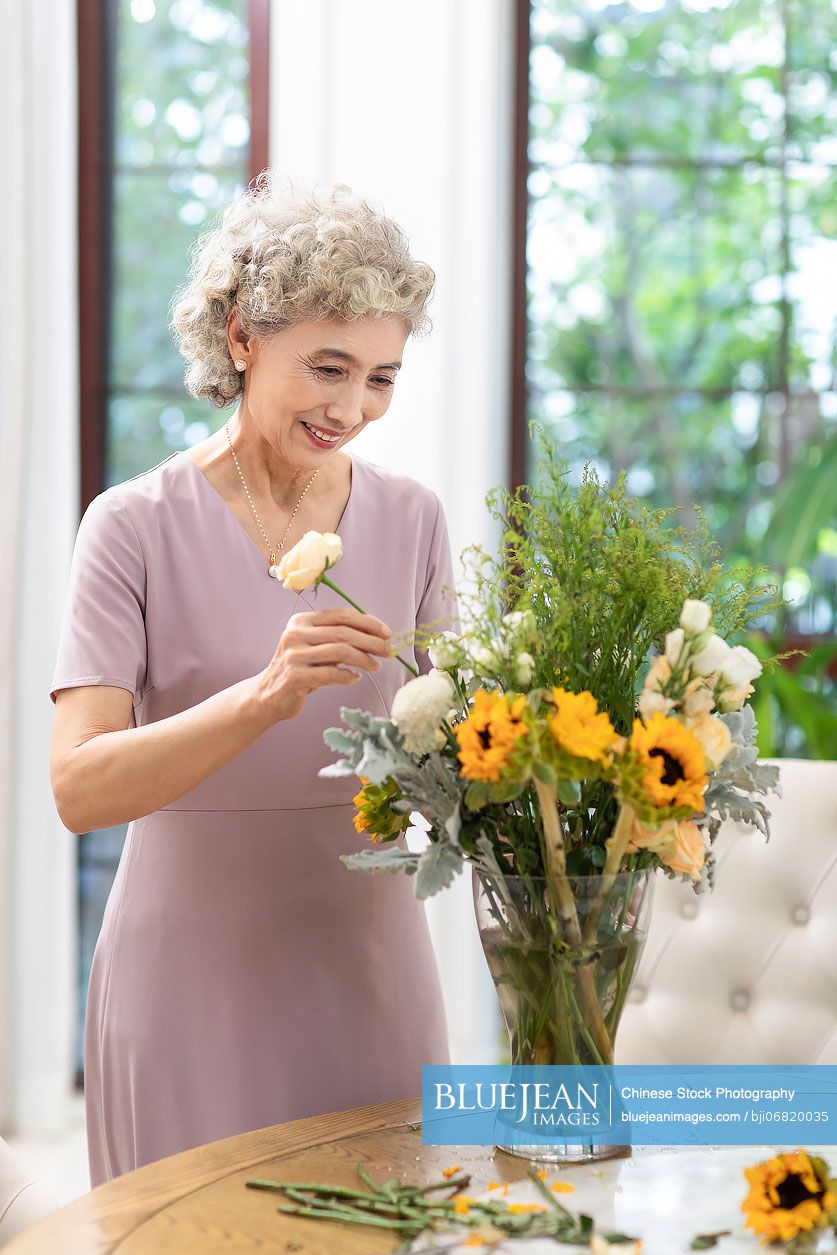 happy-senior-chinese-woman-arranging-flowers-at-home-high-res-stock