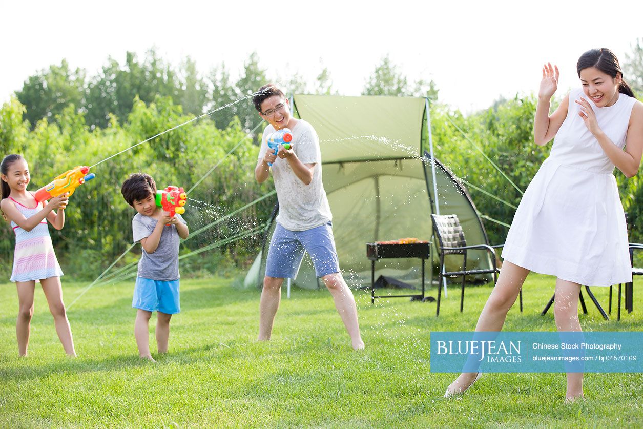 Happy young Chinese family playing squirt guns