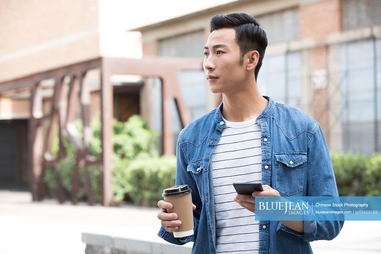 Young Chinese man holding a cup of coffee and a smart phone